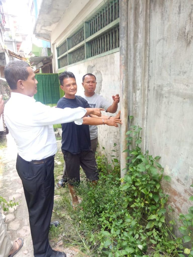 Pelaku (tengah) menunjukkan tiang bagian belakang rumah korban. (mimbar/ist)